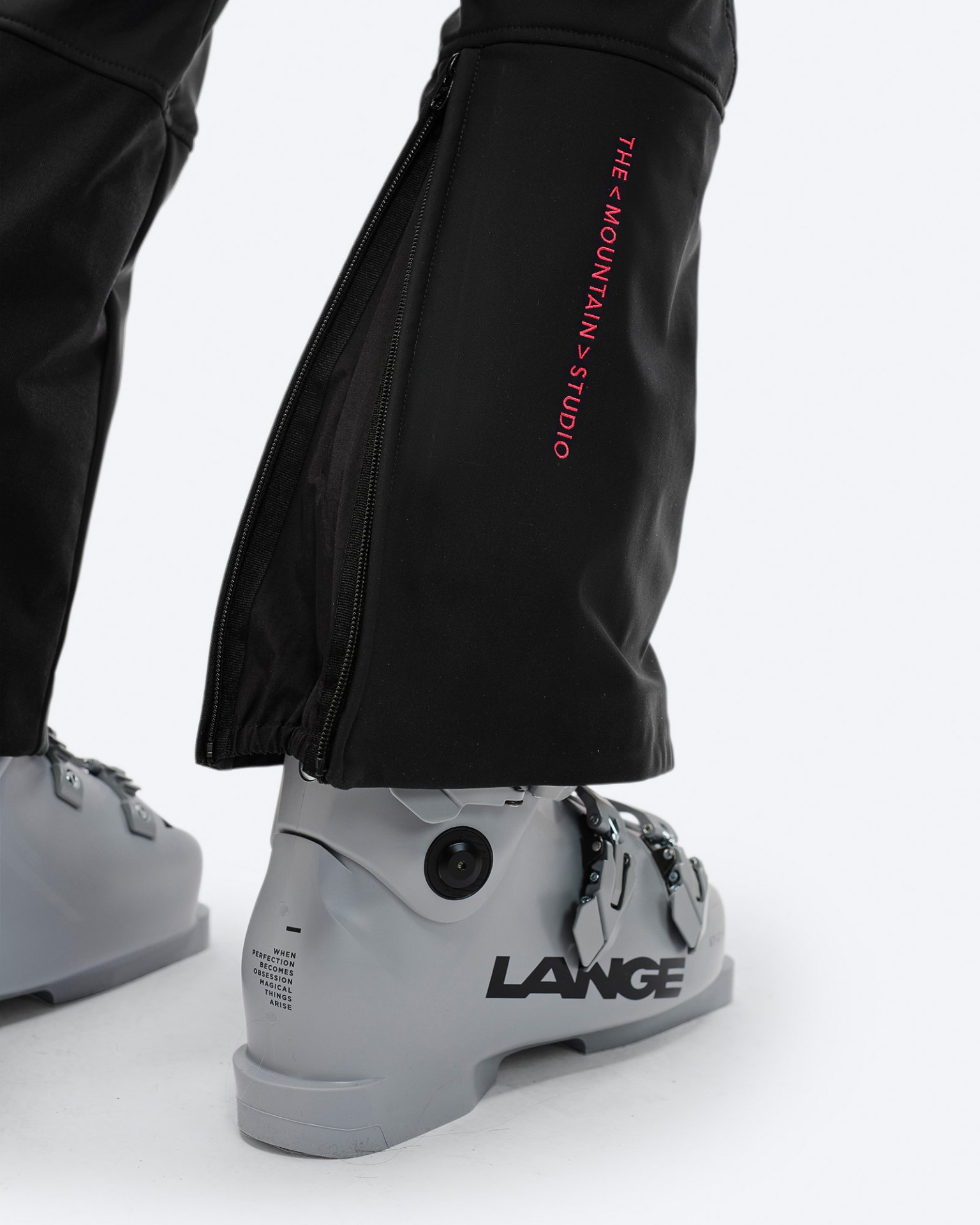 Schwarze Stretch-Skihose Nahaufnahme einer schwarzen Stretch-Skihose über einem grauen Skischuh mit Reißverschluss und Markenlogo.