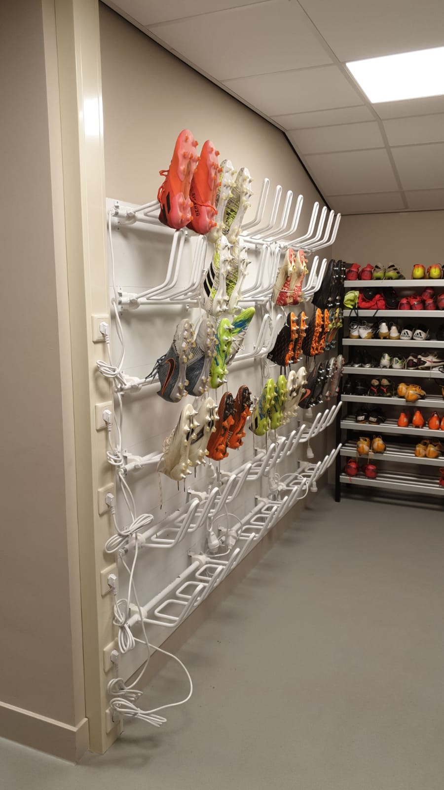 Ein Alpenheat Radiator AD8-S Schuhtrockner an einer Wand, mit Fußballschuhen auf Trocknungsstäben. Im Hintergrund ein Schuhregal.