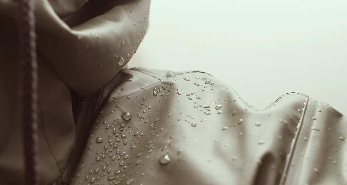 Nahaufnahme einer wasserabweisenden Jacke mit Kapuze, auf der Wassertropfen liegen.