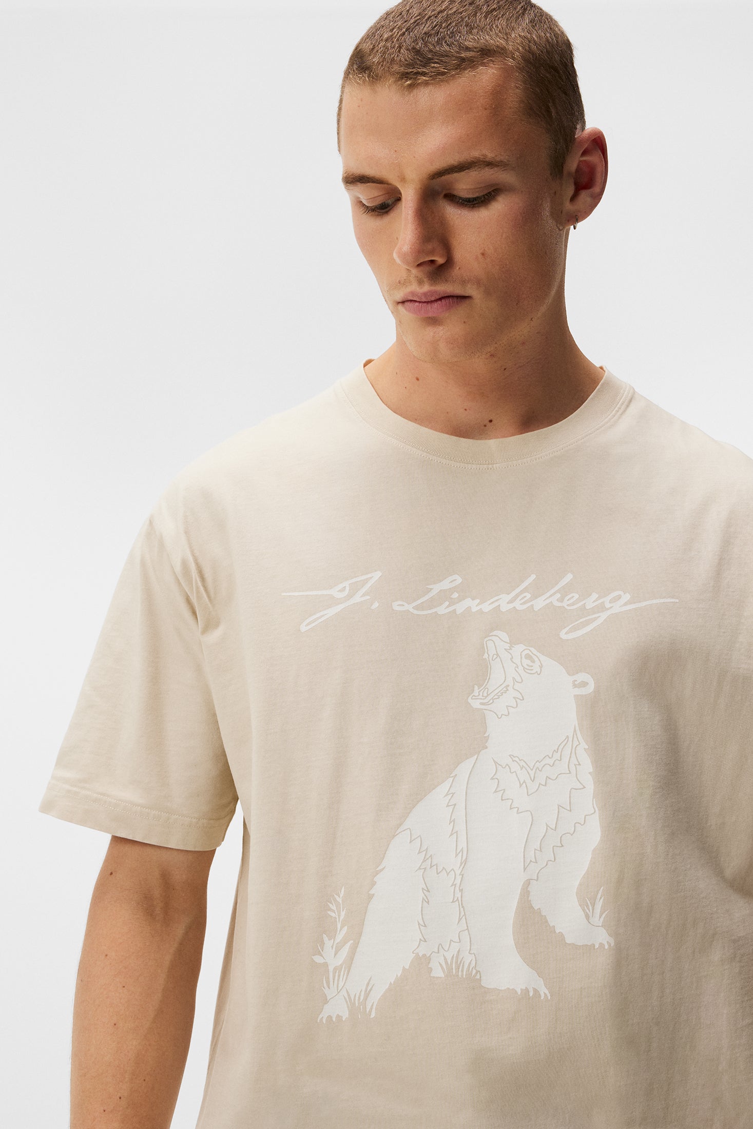 Ein Model trägt das Walsh Boxy Print Tee in Oyster Gray mit einem weißen Bären-Print und J.Lindeberg Schriftzug.