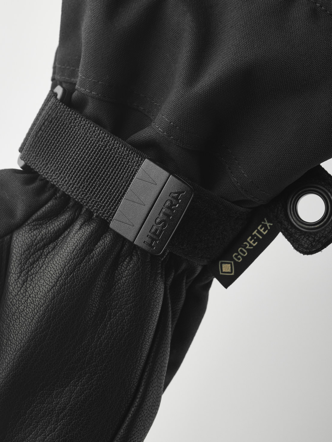 Schwarze Hestra-Handschuhe Nahaufnahme eines schwarzen Hestra-Handschuhs mit Gore-Tex-Etikett und verstellbarem Riemen. Das Material ist Leder und Textil.
