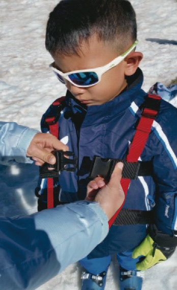 Kind mit Skibrille Kind mit Skibrille und Skitrainer-Gurt, der von einer Person geschlossen wird.