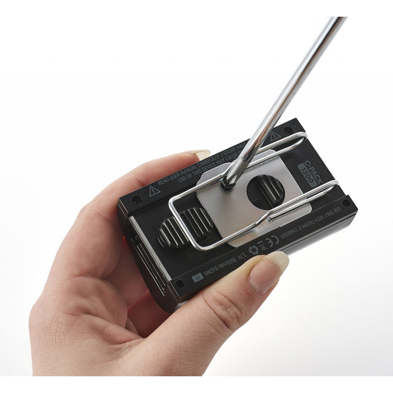 La main tient une batterie C-Pack noire avec un clip filaire en métal monté.