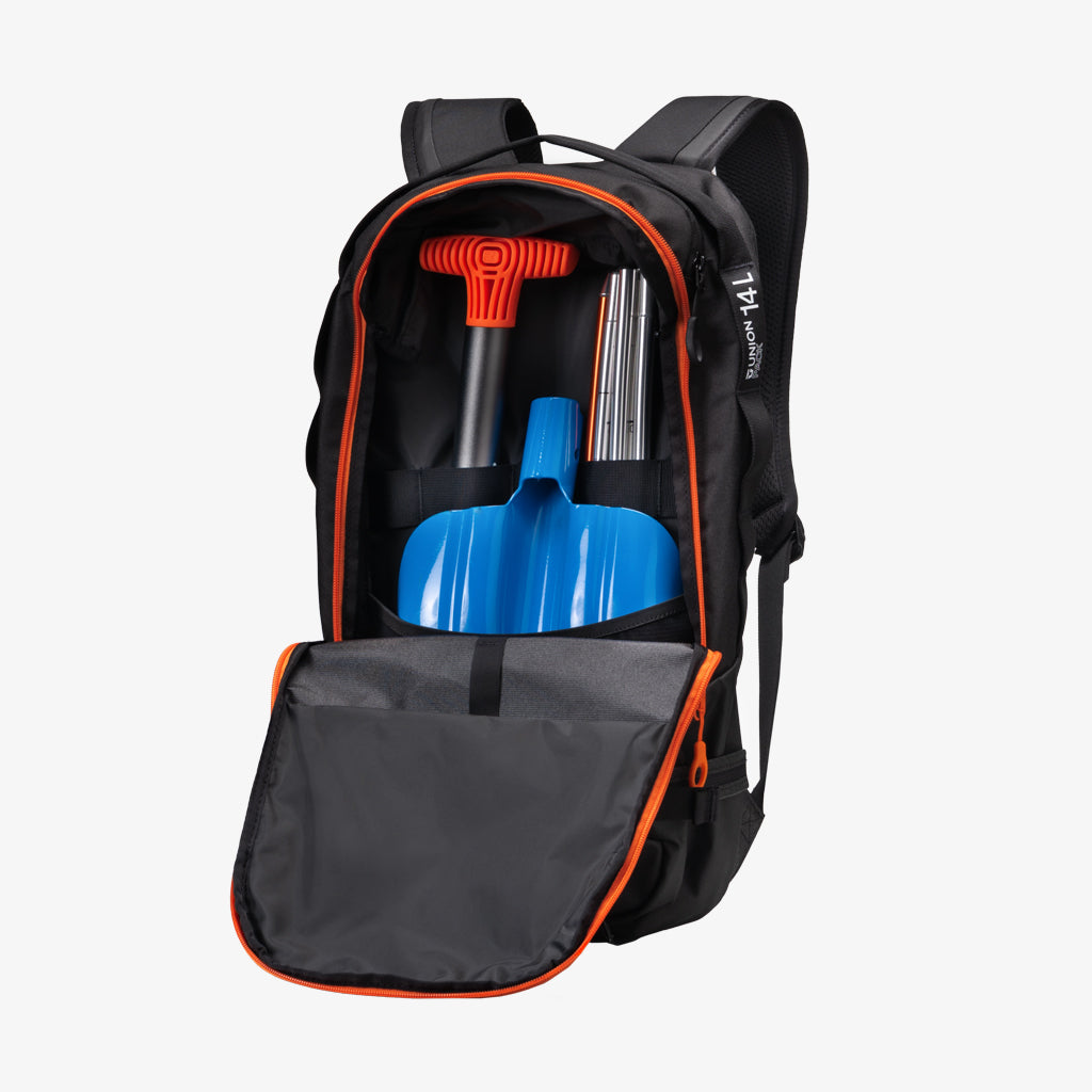 Schwarzer Rucksack mit Ausrüstung Schwarzer Union Resort Pack 14L Rucksack, offen, mit Lawinenausrüstung (Schaufel, Sonde, Spaten) im Inneren. Orangefarbene Akzente.