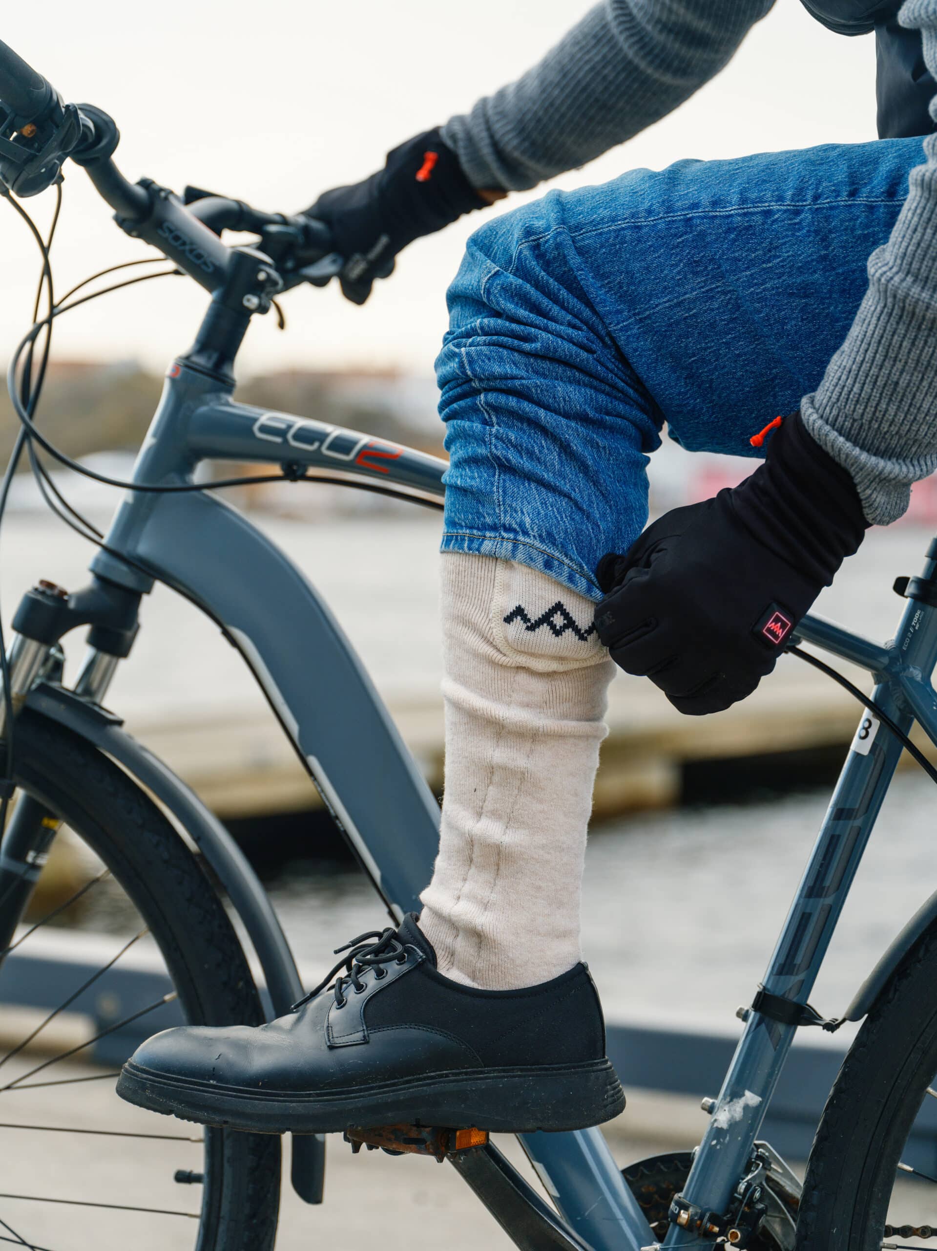Beheizte Socken und Handschuhe Person mit beheizten Socken und Handschuhen auf einem Fahrrad. Die Socke ist beige mit einem dunklen Zickzackmuster.