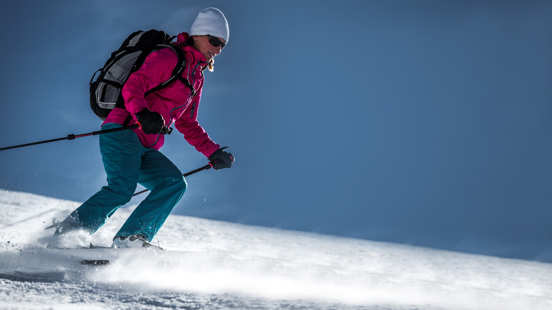 Schneeschuhfahren im Schnee Frau mit Rucksack und Skistöcken fährt mit Crossblades Softboot Schneeschuhen einen verschneiten Hang hinunter.