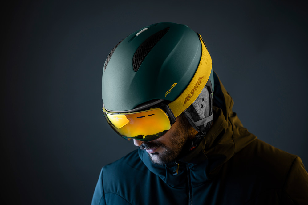 Skibrille und Skihelm Mann mit Skihelm und gelber Brille blickt nach unten; dunkler Hintergrund.