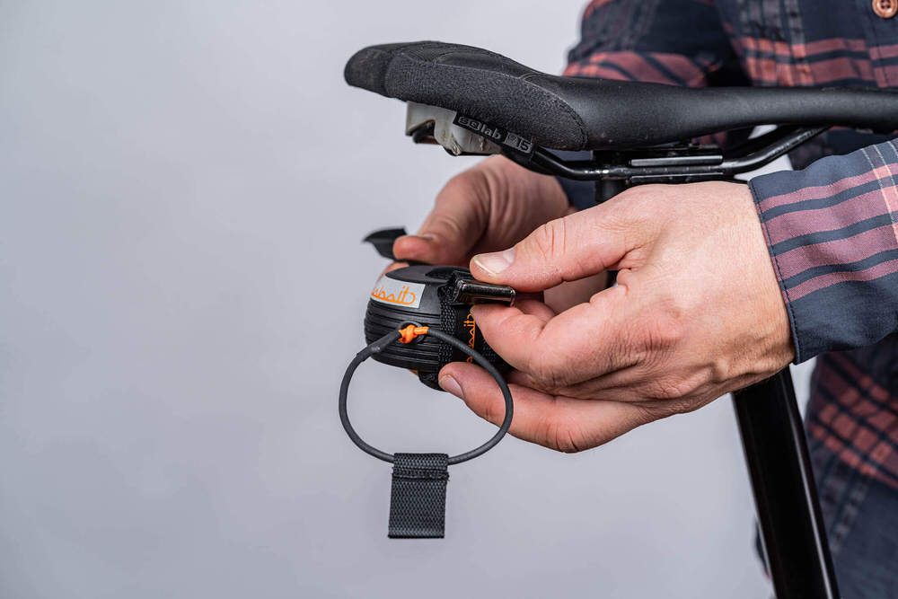 Nahaufnahme: Person befestigt kommit-Zugsystem unter einem Fahrradsattel. Das System hat ein Zugseil und eine Halterung.