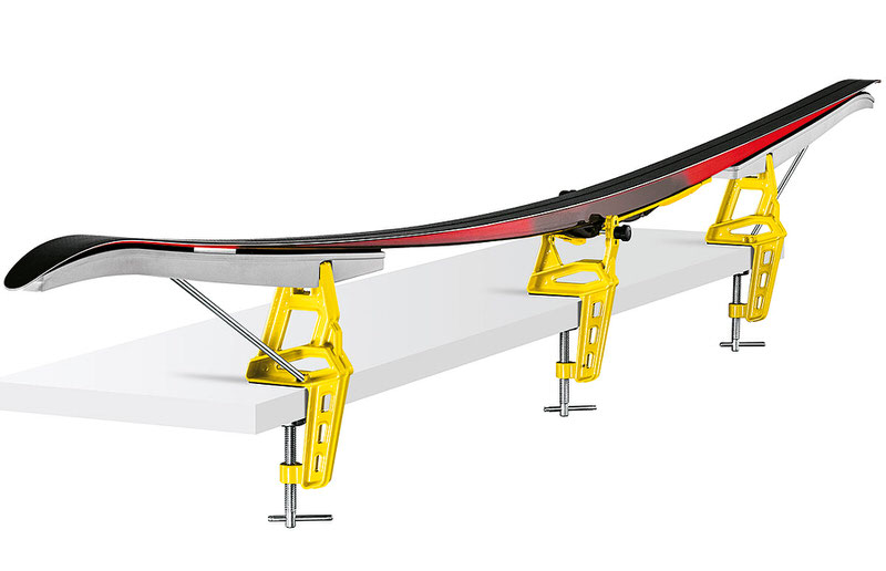 Langlaufski eingespannt in gelbem dreiteiligem Ski-Spannsystem auf einer weissen Oberfläche.