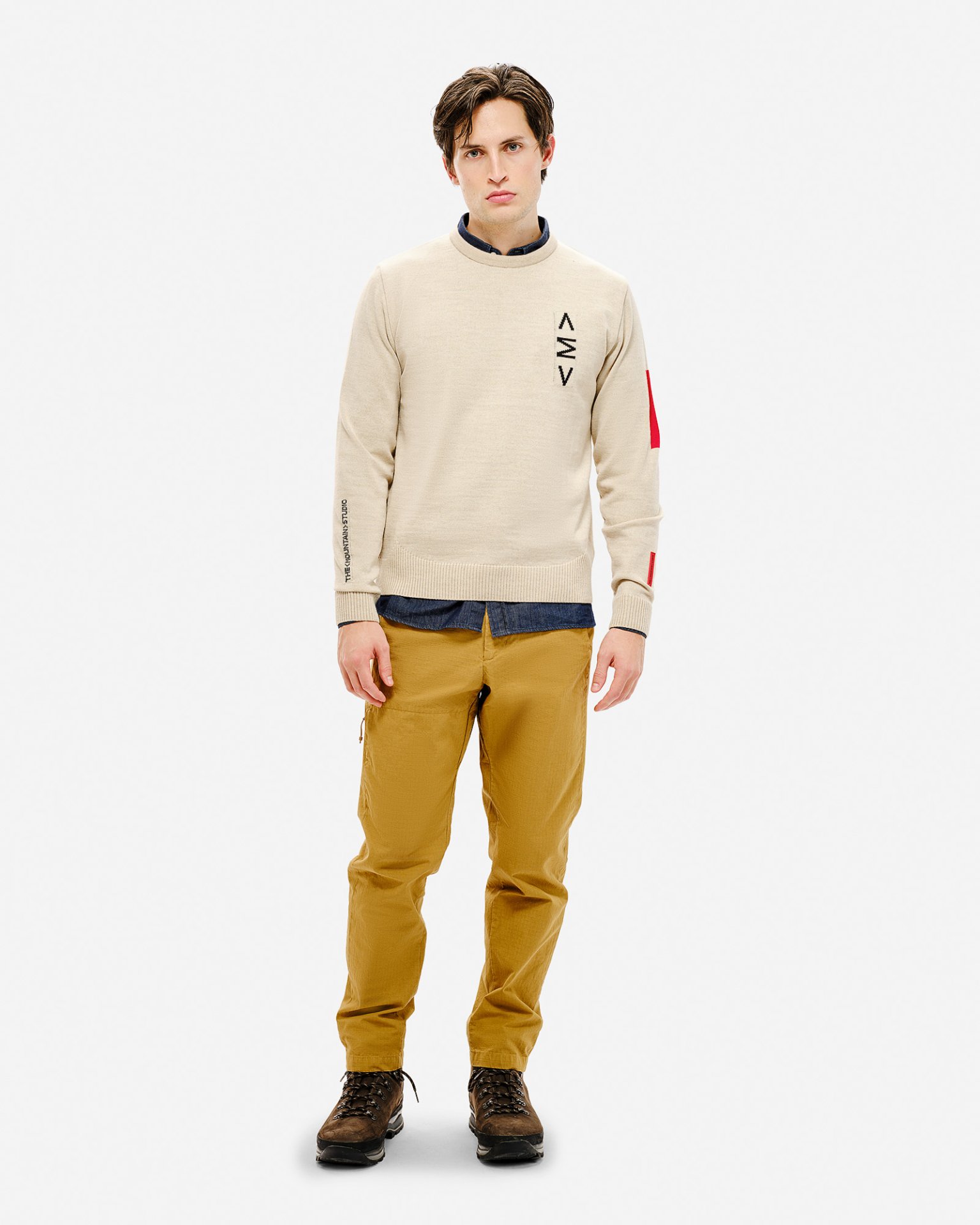 Beiger Ski Sweater Mann trägt beigen Ski Sweater mit Muster, braune Hose und Schuhe vor einem weißen Hintergrund.