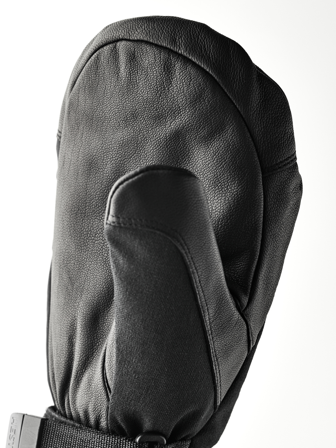 Schwarzer Lederhandschuh Eine schwarze, lederne Fäustlingshandschuh liegt auf einer weißen Fläche. Der Daumen ist nach vorne gerichtet und der Handrücken ist gewölbt.