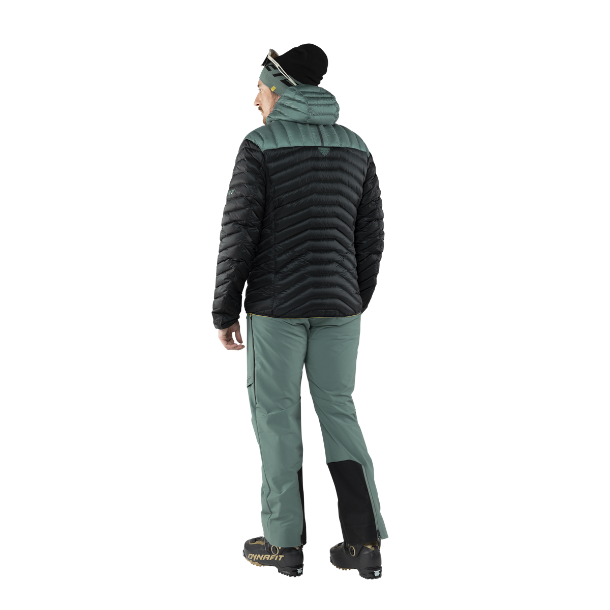 Rückansicht: Person mit Dynafit Ridge Ultralight Daunenjacke in Schwarz und Grün. Ski-Hose, Mütze und Skischuhe.