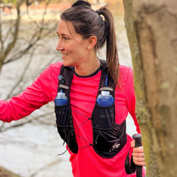 Läuferin mit Trinkweste Läuferin mit Trinkweste Hydrabag Elite 8L und zwei blauen Trinkflaschen. Sie hält einen Trekkingstock in der Hand.