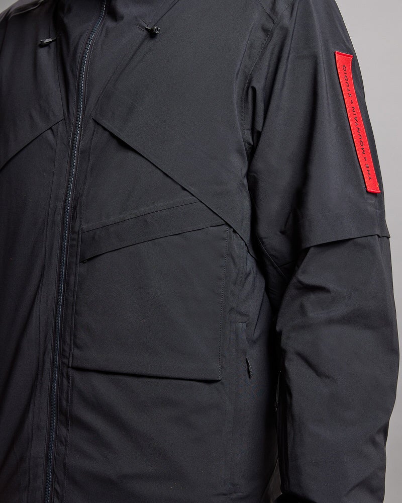 Schwarze S-1 Gore-Tex Jacke Detailaufnahme einer schwarzen S-1 Gore-Tex 2L Stretch Insulated Jacket. Sichtbar sind Taschen, Reißverschluss und Ärmel mit rotem Logo.
