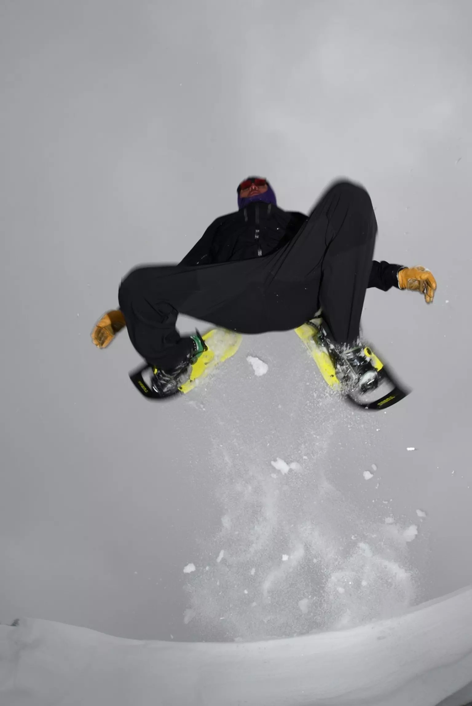 Mann auf gelben Schneeschuhen Ein Mann springt auf gelben Tubbs VRT 29 Schneeschuhen über eine schneebedeckte Oberfläche.