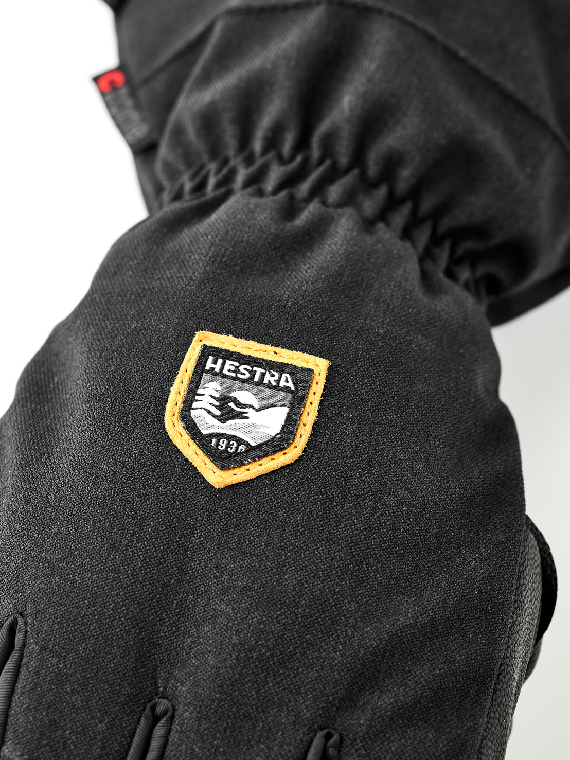 Hestra Schwarzer Handschuh Detailansicht eines schwarzen Handschuhs mit Hestra-Logo, das Berge und das Gründungsjahr 1936 zeigt.