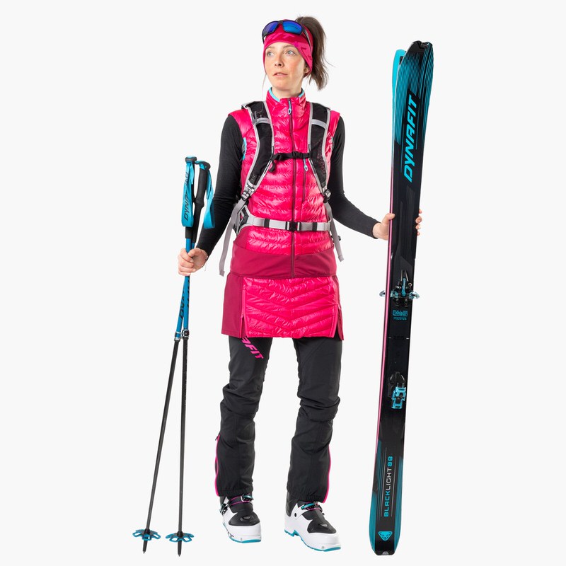 Skifahrerin mit Dynafit Skis Frau mit Dynafit Blacklight 88 Ski, Skistöcken und Skitourenbekleidung vor einem weißen Hintergrund.