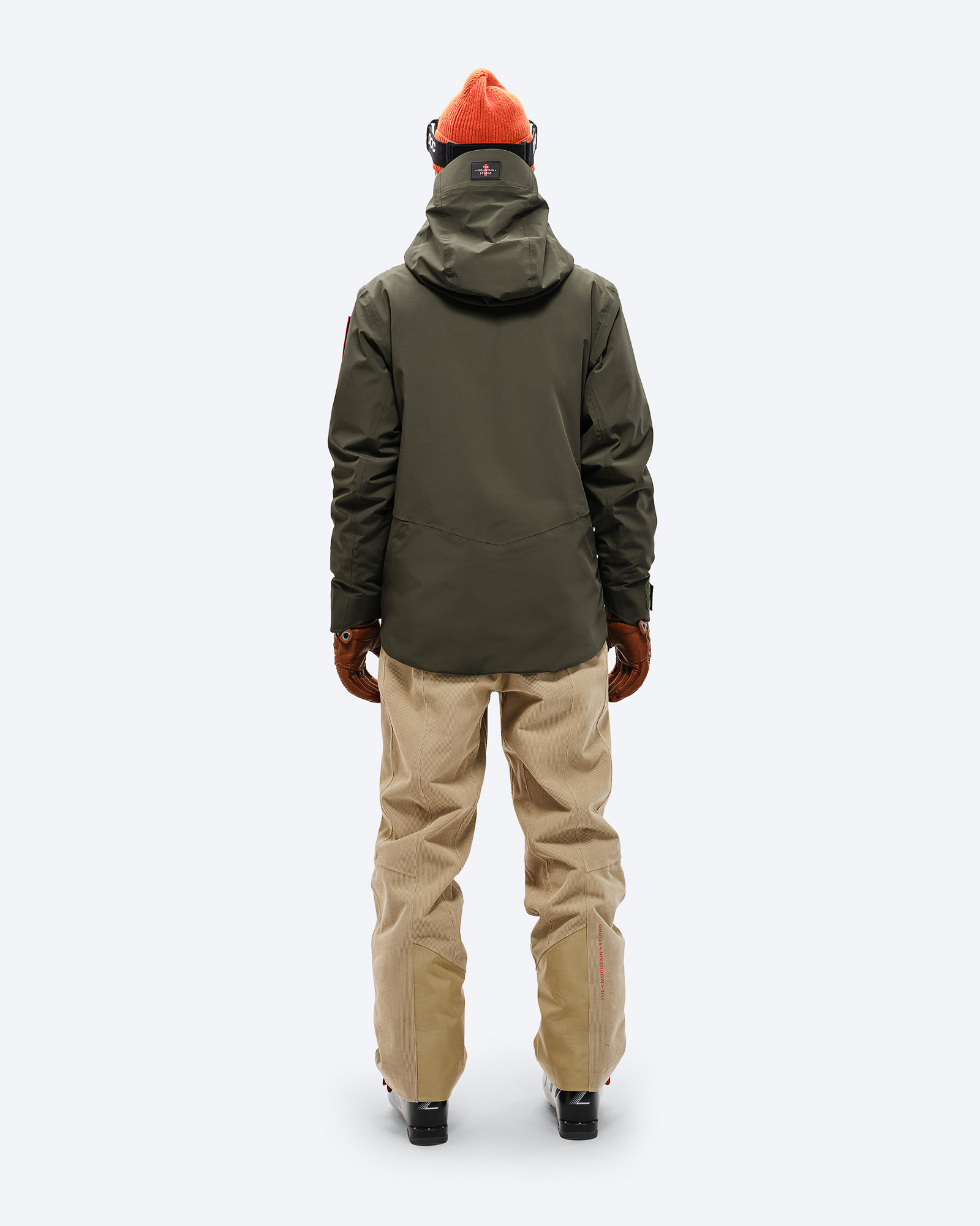 Skijacke in Waldgrün Rückenansicht einer Person in Forest Green S-3 Carv Insulated Stretch Jacket mit Skibrille, Mütze, Handschuhen, Hose und Skischuhen.