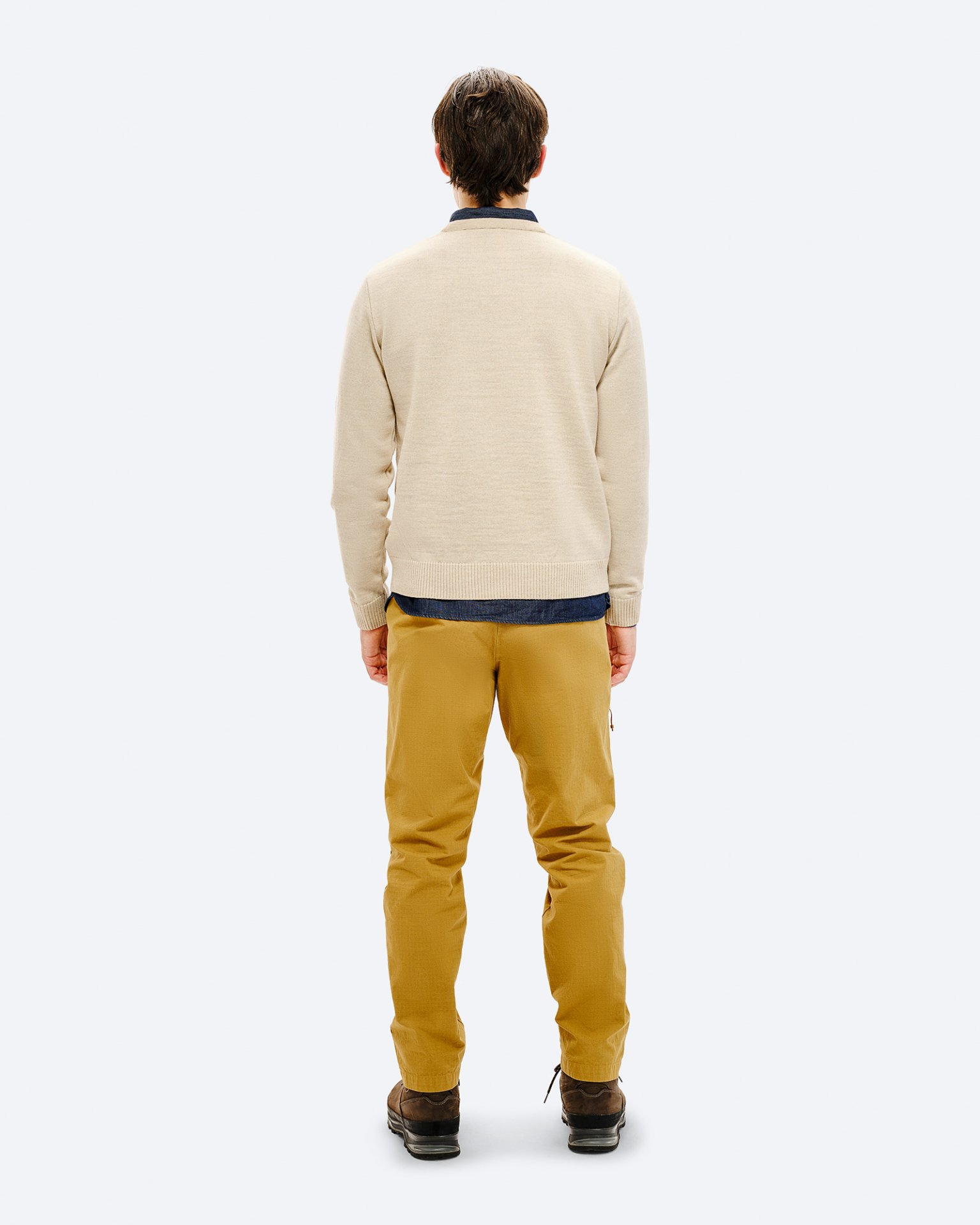 Mann im Ski-Outfit Rückansicht eines Mannes mit beigem Ski Sweater, gelben Hosen und braunen Schuhen vor neutralem Hintergrund.