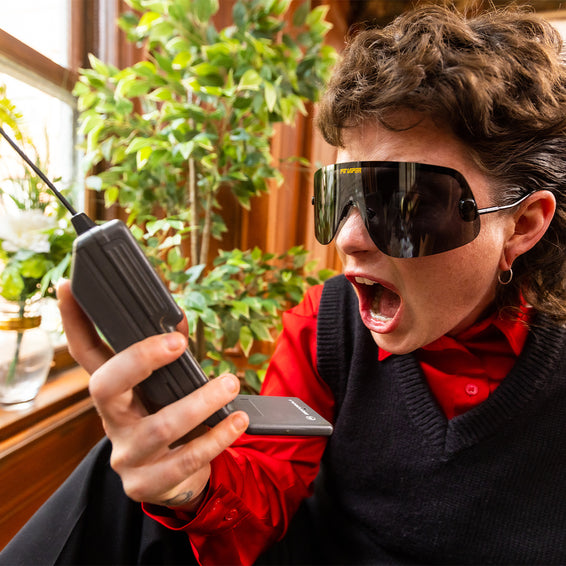 Une personne portant des lunettes de soleil polarisées tient un vieux téléphone portable et crie.