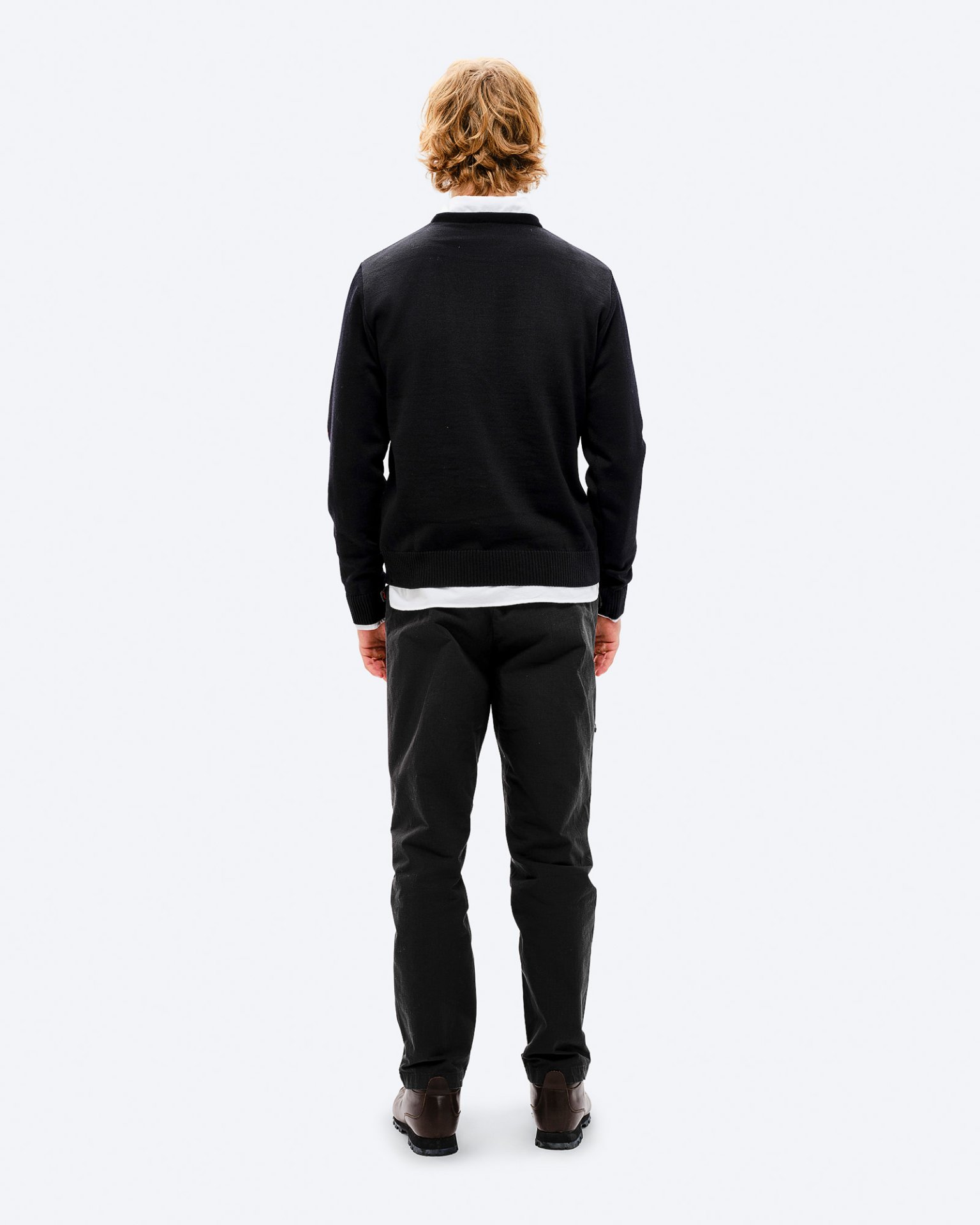 Mann im K-3 Ski Outfit Rückenansicht eines Mannes mit blonden Haaren in schwarzem K-3 Ski Sweater, Hose und Schuhen vor weißem Hintergrund.