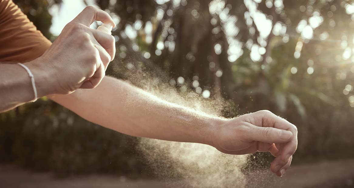 Eine Person sprüht Insektenschutzmittel auf ihren Arm im Freien.