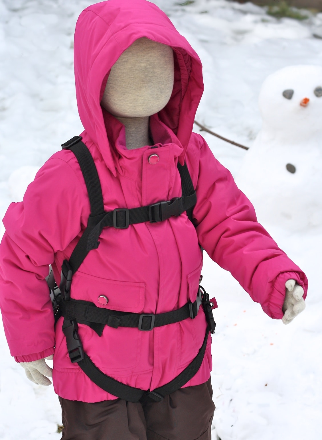 Puppe im Schnee Puppe trägt pinke Winterjacke mit Lil' Ripper Gripper Skilernhilfe im Schnee, im Hintergrund ein Schneemann.