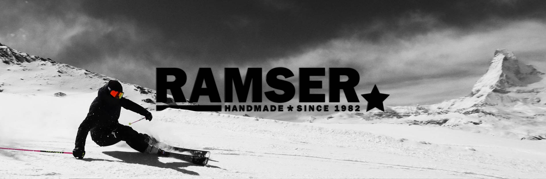 Skifahrer in Berglandschaft Skifahrer vor verschneiter Berglandschaft mit dem Schriftzug "RAMSER HANDMADE * SINCE 1982" im Zentrum des Bildes.