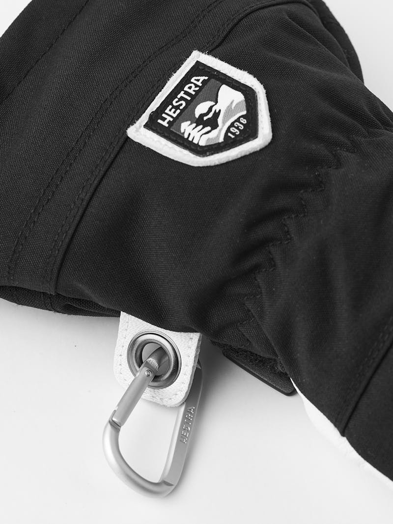 Detail einer schwarzen Hestra Army Leather Heli Ski Mitt mit Logo und Karabinerhaken.