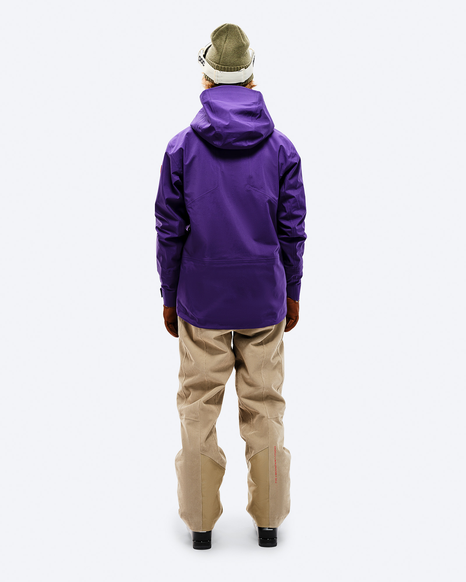 Lila GORE-TEX Jacke Person von hinten in lila GORE-TEX Shell Jacket, beigen Hosen, Mütze und Skibrille.