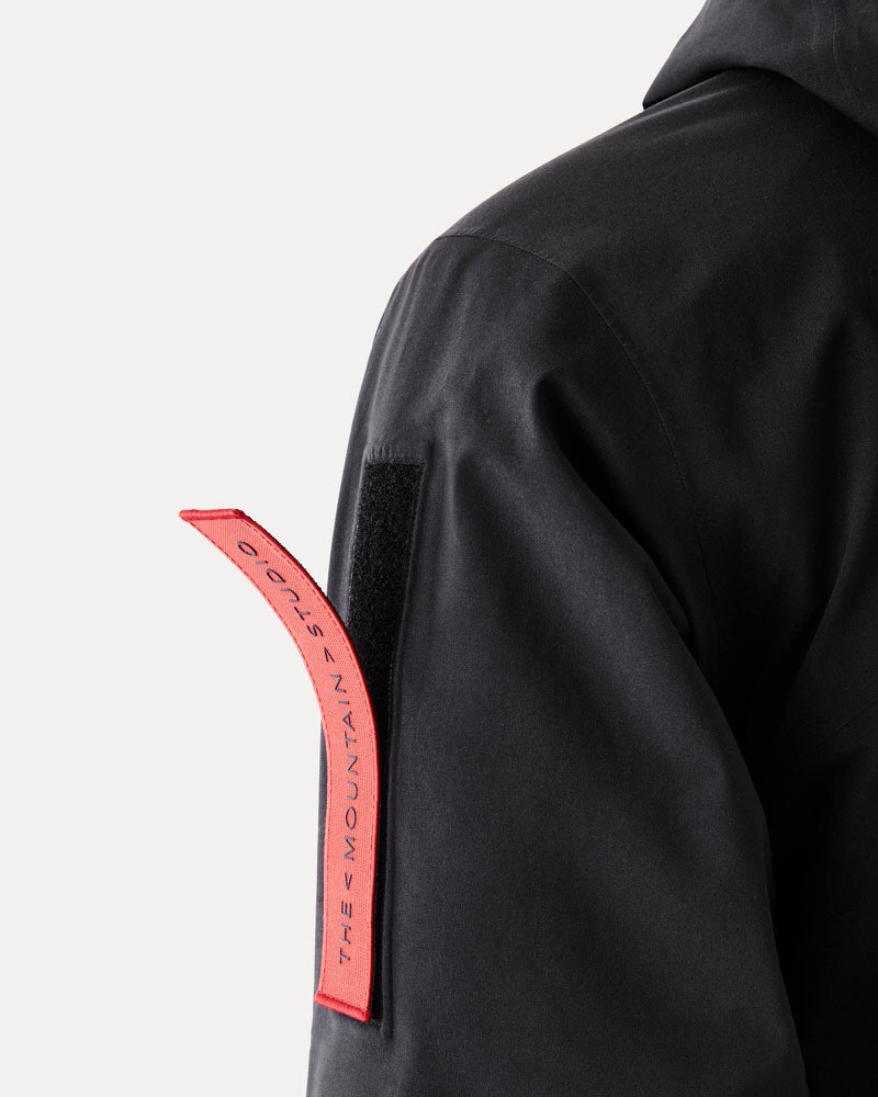 Schwarze Gore-Tex Jacke Detailaufnahme einer schwarzen Gore-Tex S-1 Jacke; Ärmel mit rotem Band mit Aufschrift "The Mountain Studio".