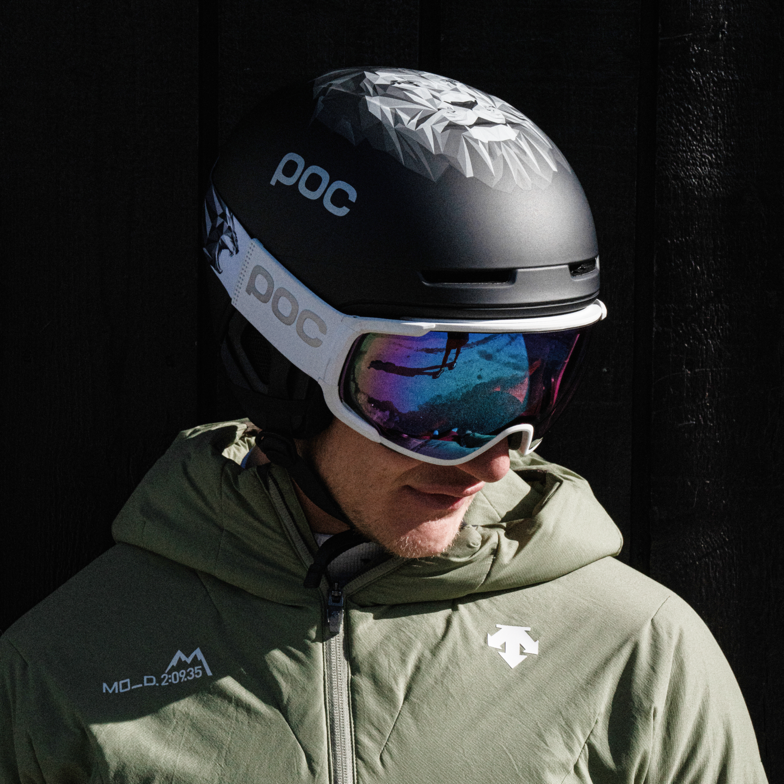 Löwen-Skihelmmann Mann mit POC Skihelm, Lwen-Motiv, und Skibrille. Reflektion in der Brille. Grüne Jacke.