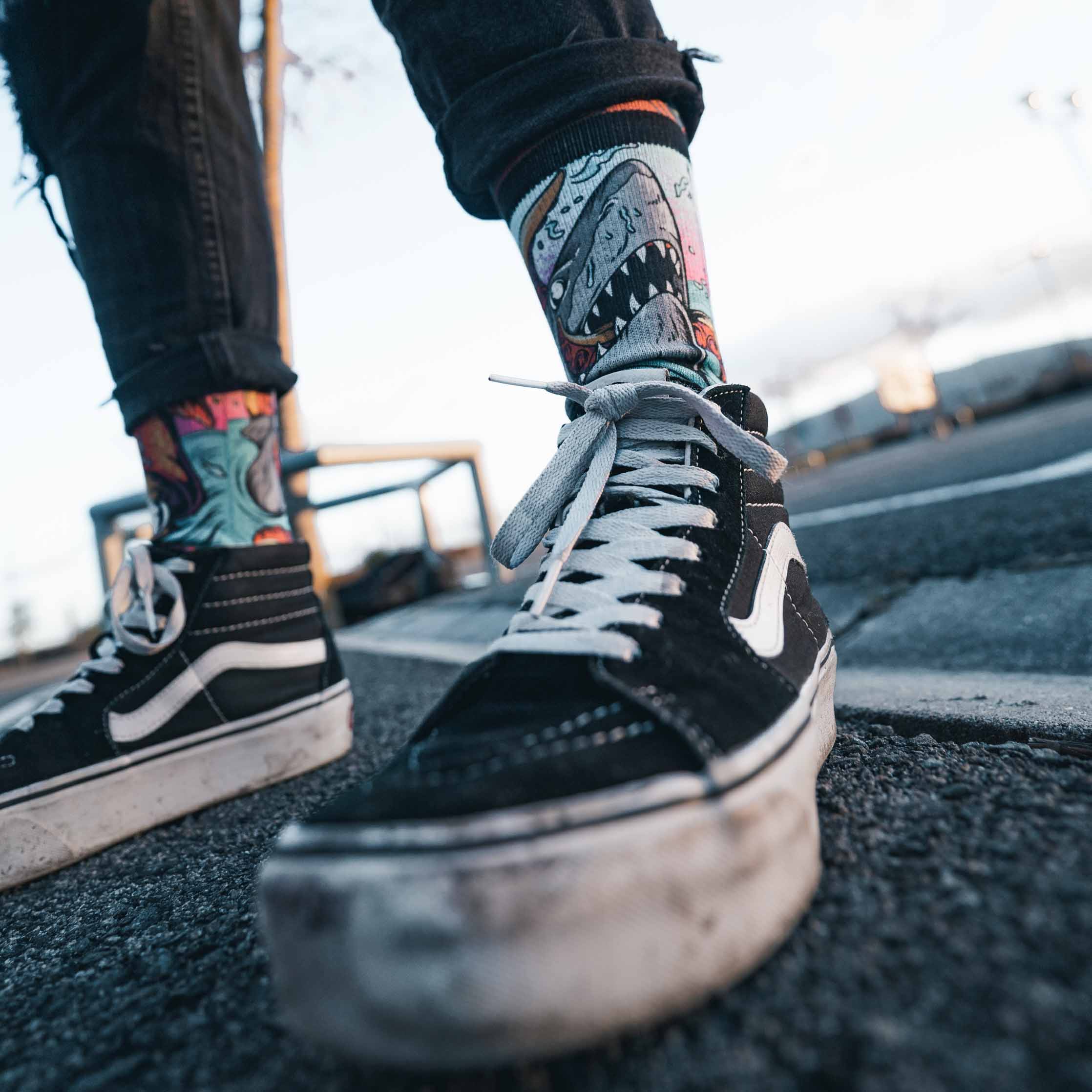 Chaussettes à motif requin Une personne portant un jean noir et des chaussures noires porte des chaussettes "Seamonsters - Mid High" à motif requin.