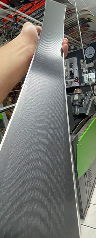 Ski mit Textur Hand hält einen Ski mit grauer, gewellter Textur vor einem Ski-Geschäft.