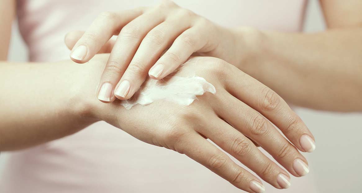Hände einer Person, die sich Handcreme auf den Handrücken aufträgt. Die Nägel sind gepflegt.