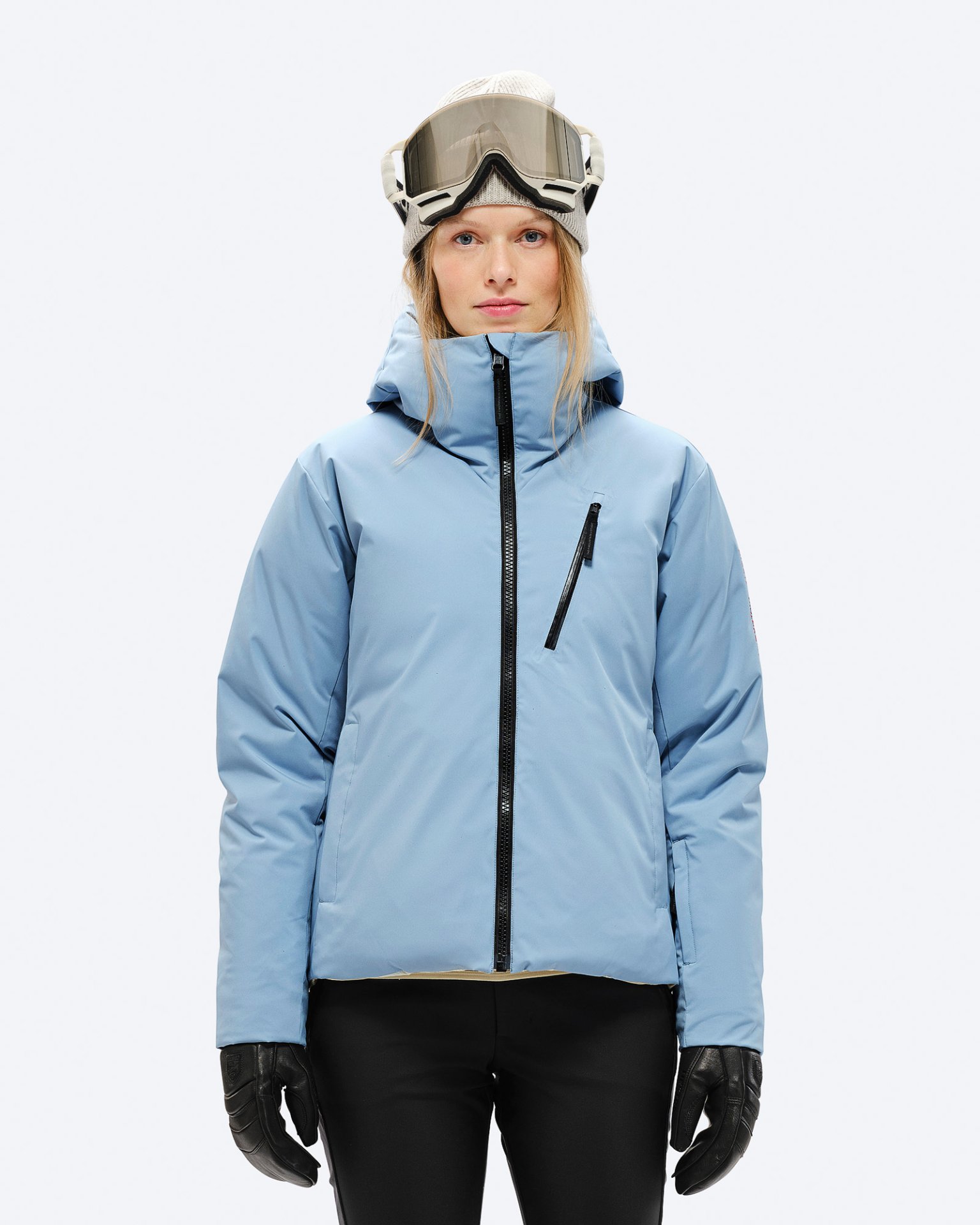 Damen Skijacke Eine Frau mit Mütze und Skibrille trägt eine hellblaue Daunenjacke mit Kapuze und schwarzem Reißverschluss.