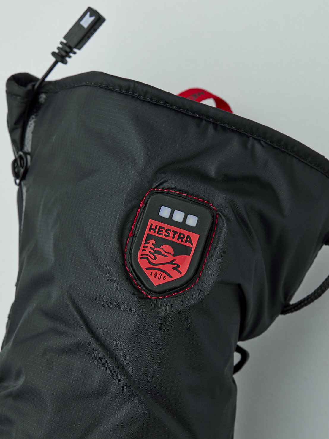 Nahaufnahme eines schwarzen beheizbaren Handschuhfutters der Marke Hestra mit USB-Anschluss und Logo.